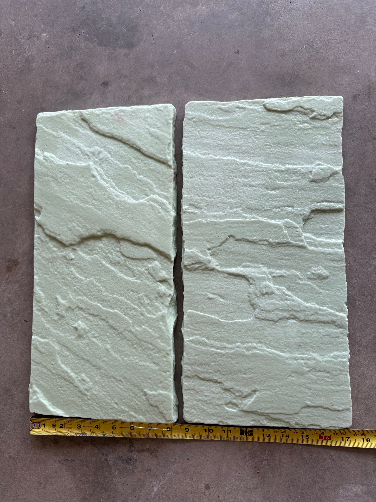 Two stone Slate stamps with a ruler for scale on a gray surface
