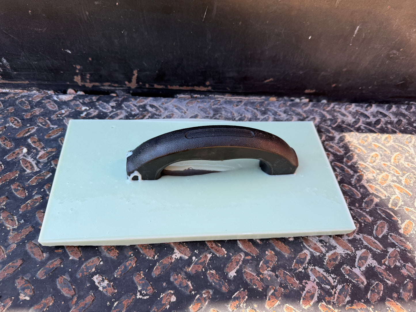 light green rectangle trowel laying on its back to show the handle. On top of a black metal plate.