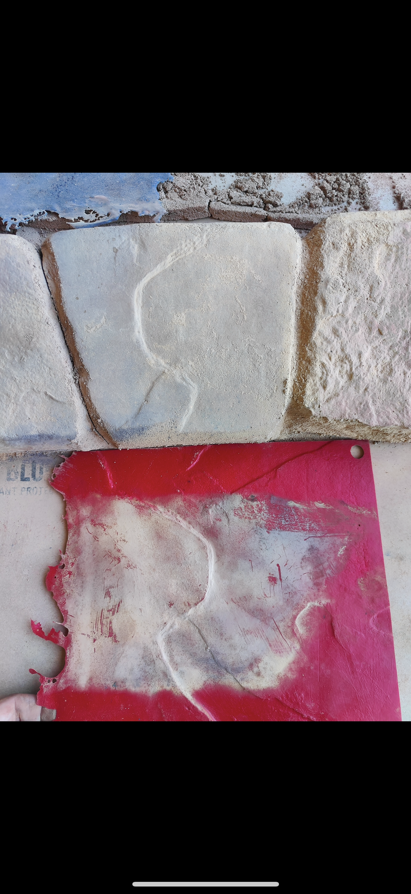 Close-up of a red concrete curbing sandstone stamp with natural stone texture placed below a real stone surface. The stamp captures the stone's details, including cracks and indentations. The edges of the stamp appear worn and slightly torn, and fine dust of the stamping process is visible. The image highlights the comparison between the stamped concrete impression and the original stone texture.