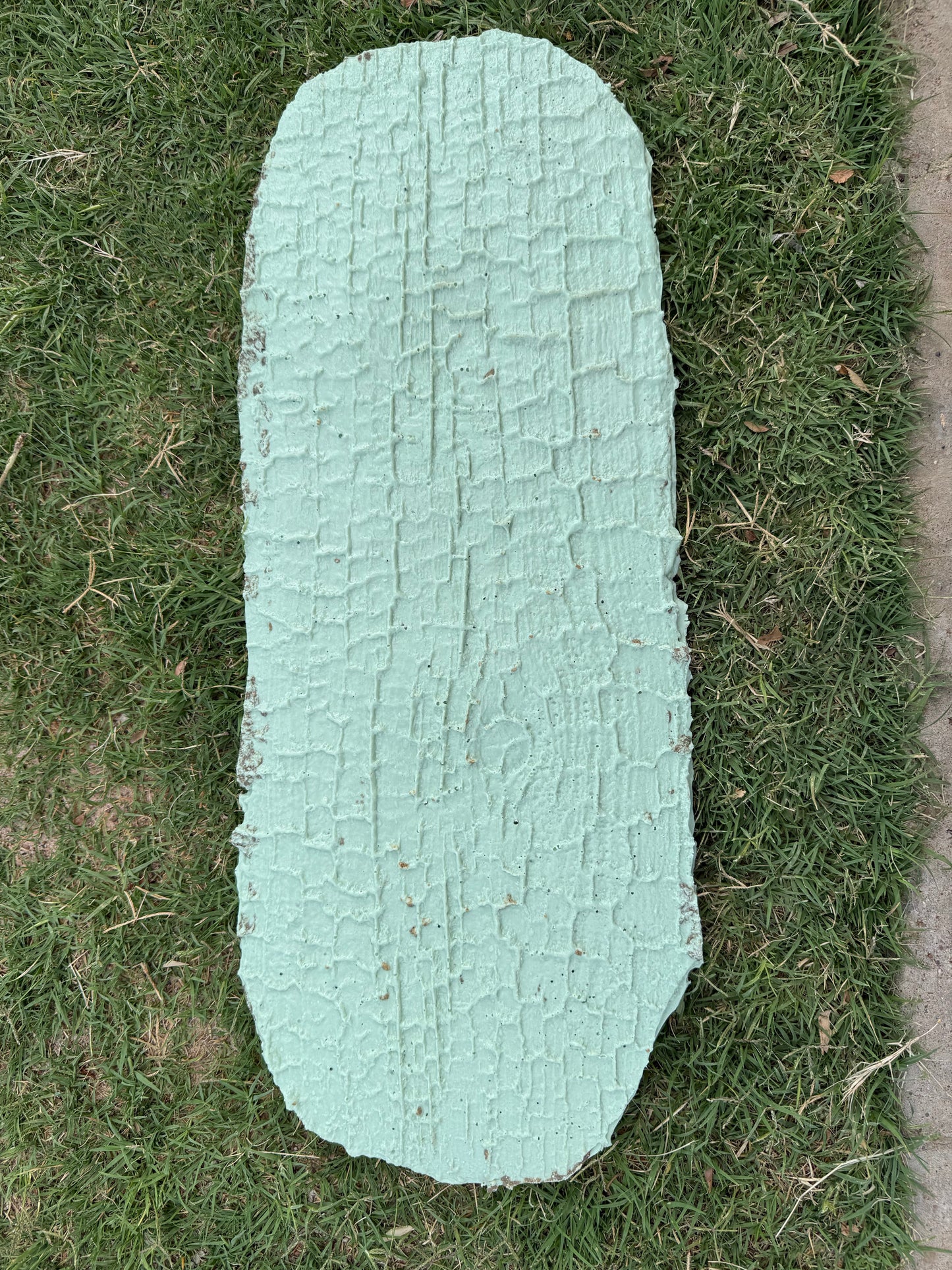 Smoke Trail Timber cement stamp light green in color on top of some grass. the stamps shows burnt wood texture.