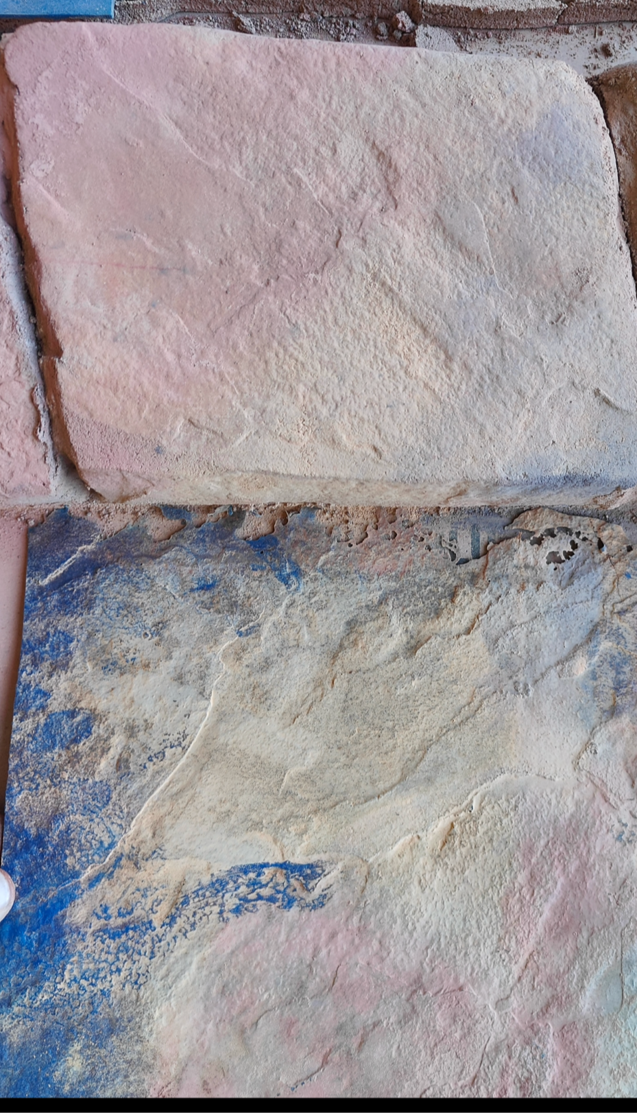 close-up of a textured concrete stamp sample place in front of a natural stone surface. The stamp mimics the rough texture and color variations of the stone above it, with shades of beige,
pink, and subtle blue tones. the edges of the tamp are slightly irregular, and fine dust from the stamping process in visible. The image captures a detailed comparison between he stamped concrete and the actual stone texture.