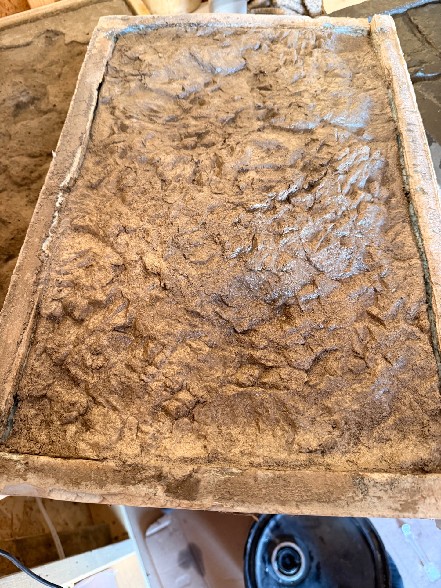 Textured canyon ledge concrete stamp surface on a wooden board with a power tool in the background