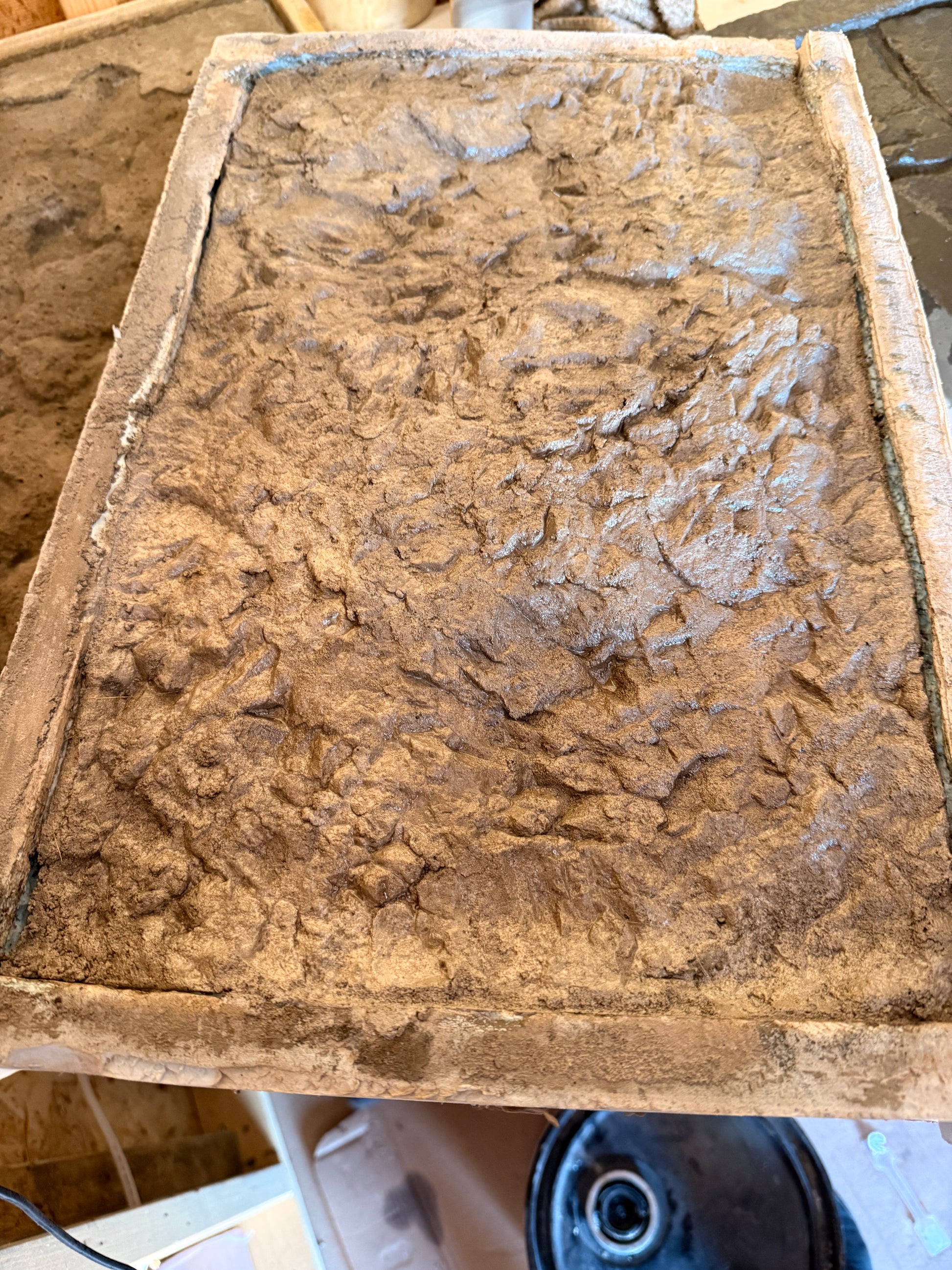 Textured canyon ledge concrete stamp surface on a wooden board with a power tool in the background