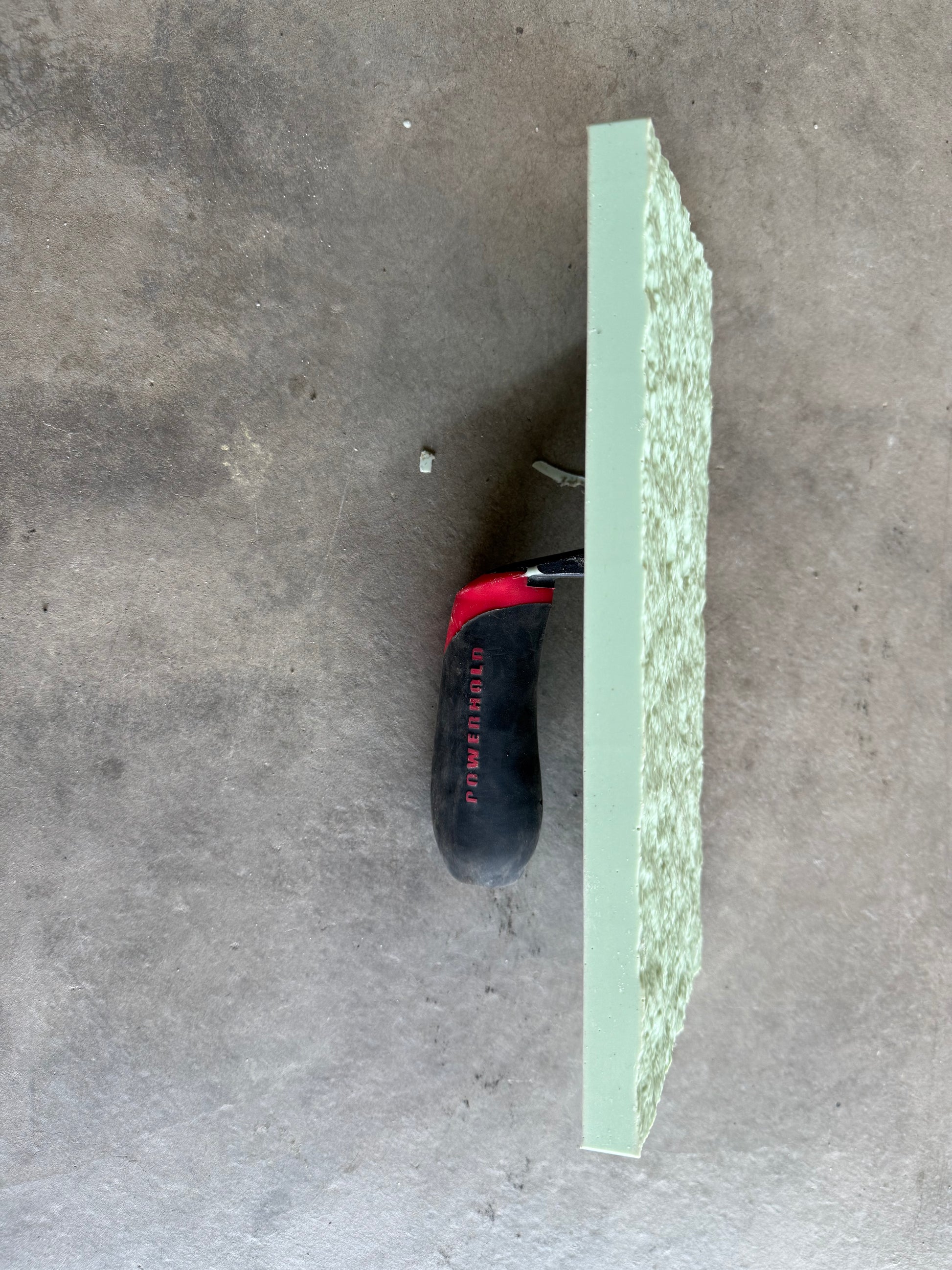 cobble stone trowel on  a concrete floor on its side to show details it also has a handle attached to it.