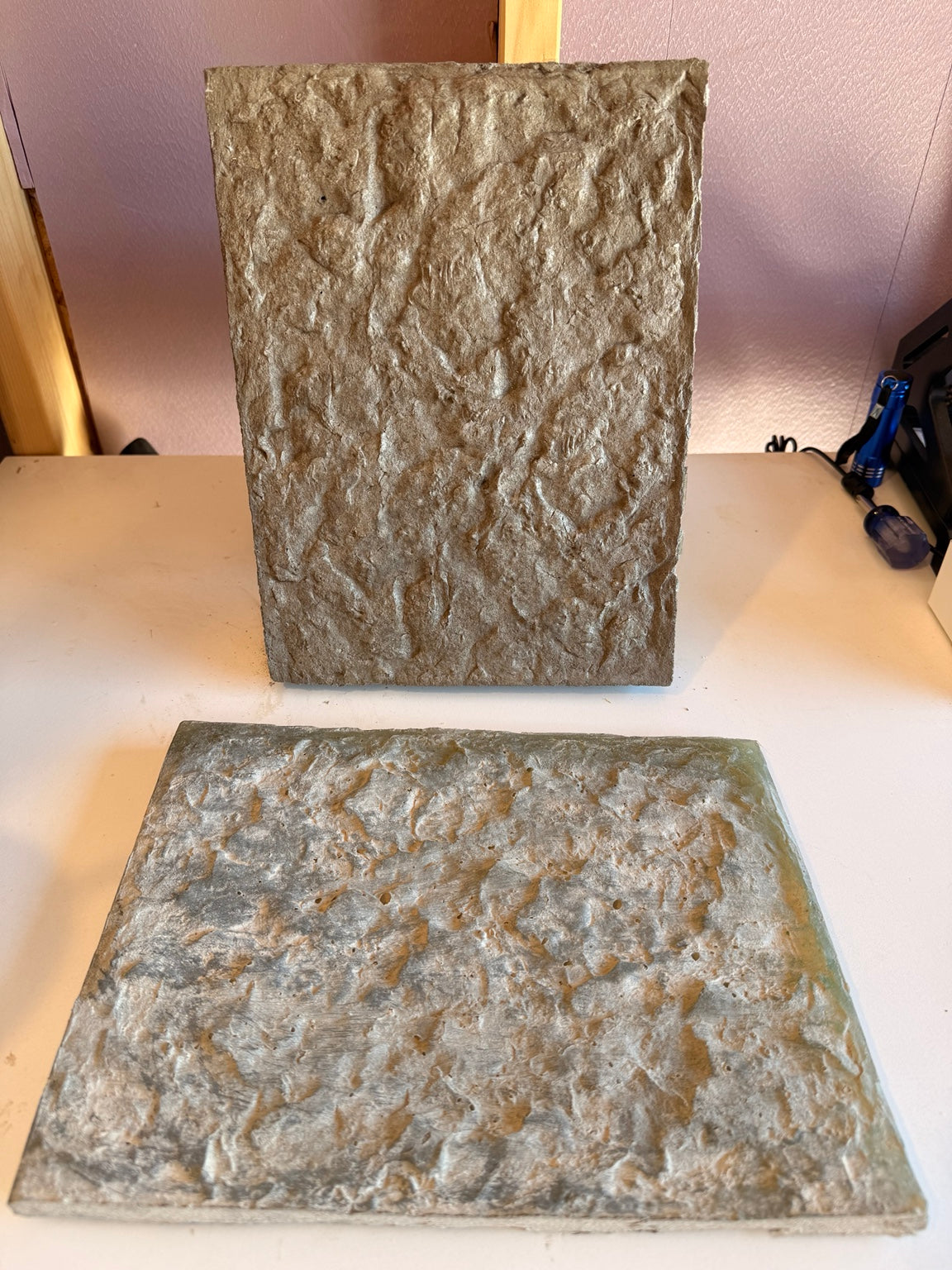 Two stone-like tiles on a white surface with a neutral background