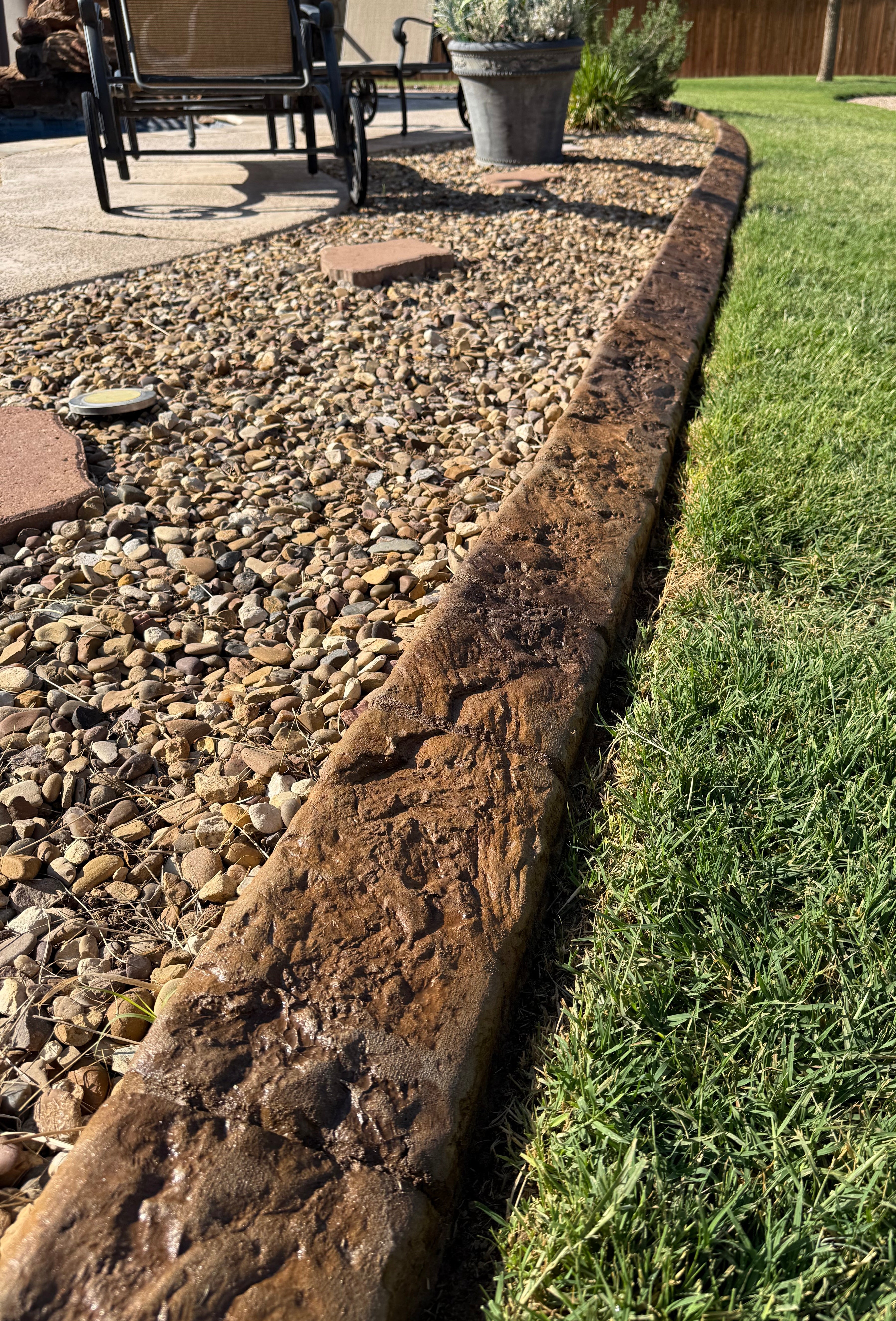 Onyx Series 2pc stamps shown on landscape curbing next to some rock and grass. the curbing has brown earthy tones with deep texture.