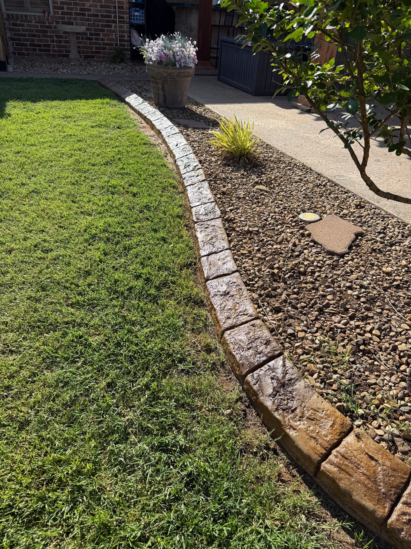 Garden area with stone border, grass, and a paved path.