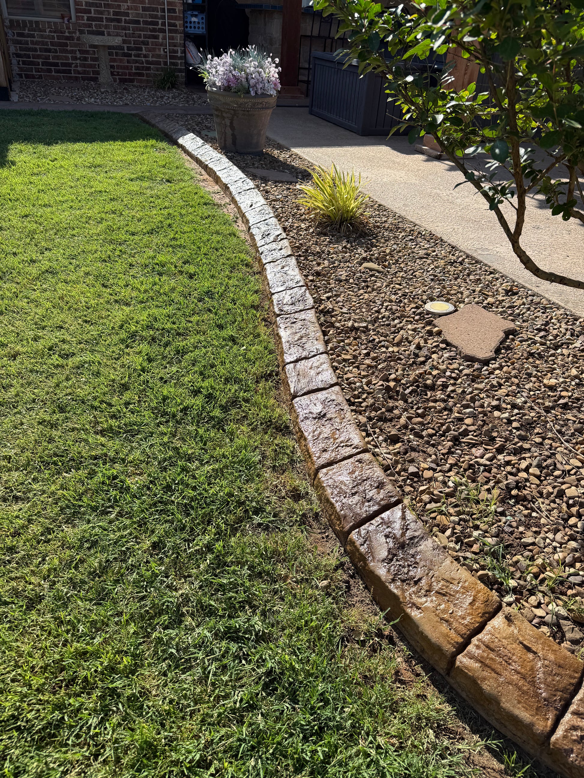 Garden area with stone border, grass, and a paved path.