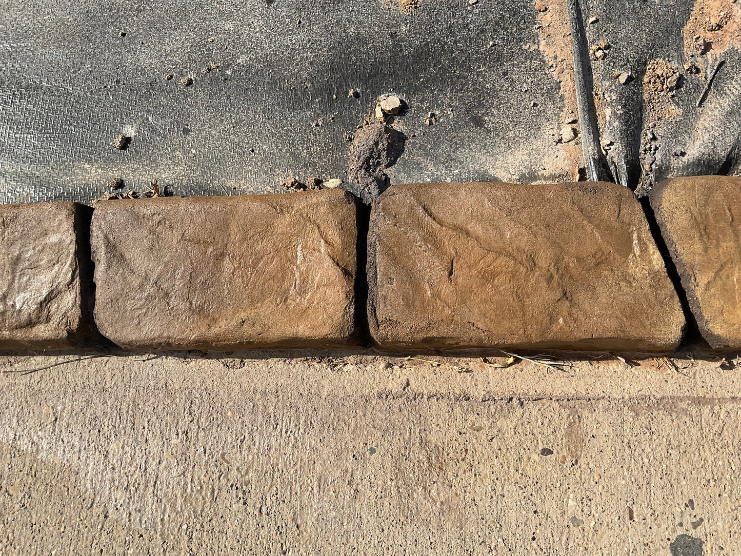 Palo Duro slate curb brown earth tones in color with black deep joint lines along a concrete walkway top view black weed barrier on the back side of curb Curbart Creations