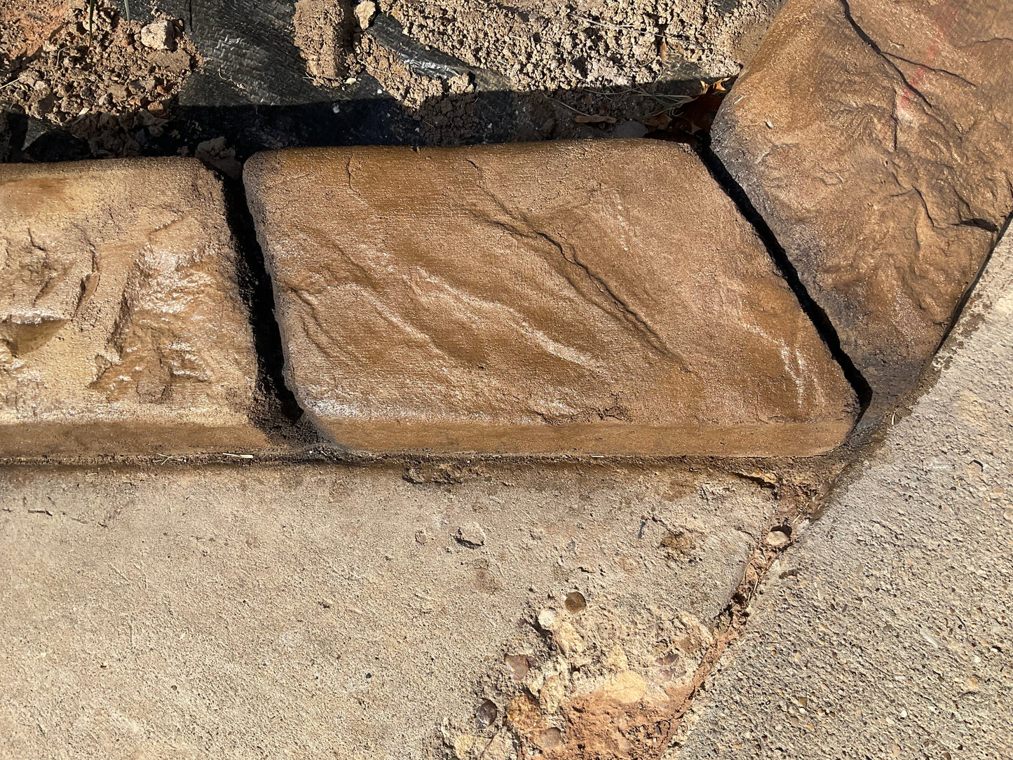 Palo Duro slate brown earth tones in color with black deep joint lines along a concrete walkway top view showing texture of curb. Curbart Creations