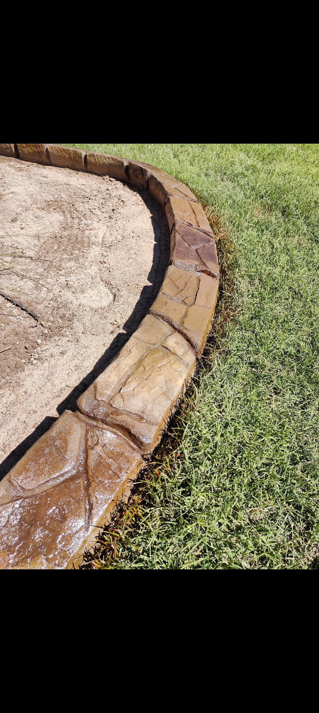 brown earth tone curved curb along some green grass next to a flower bed top view shows the deep stone like textures that mimic natural stone.