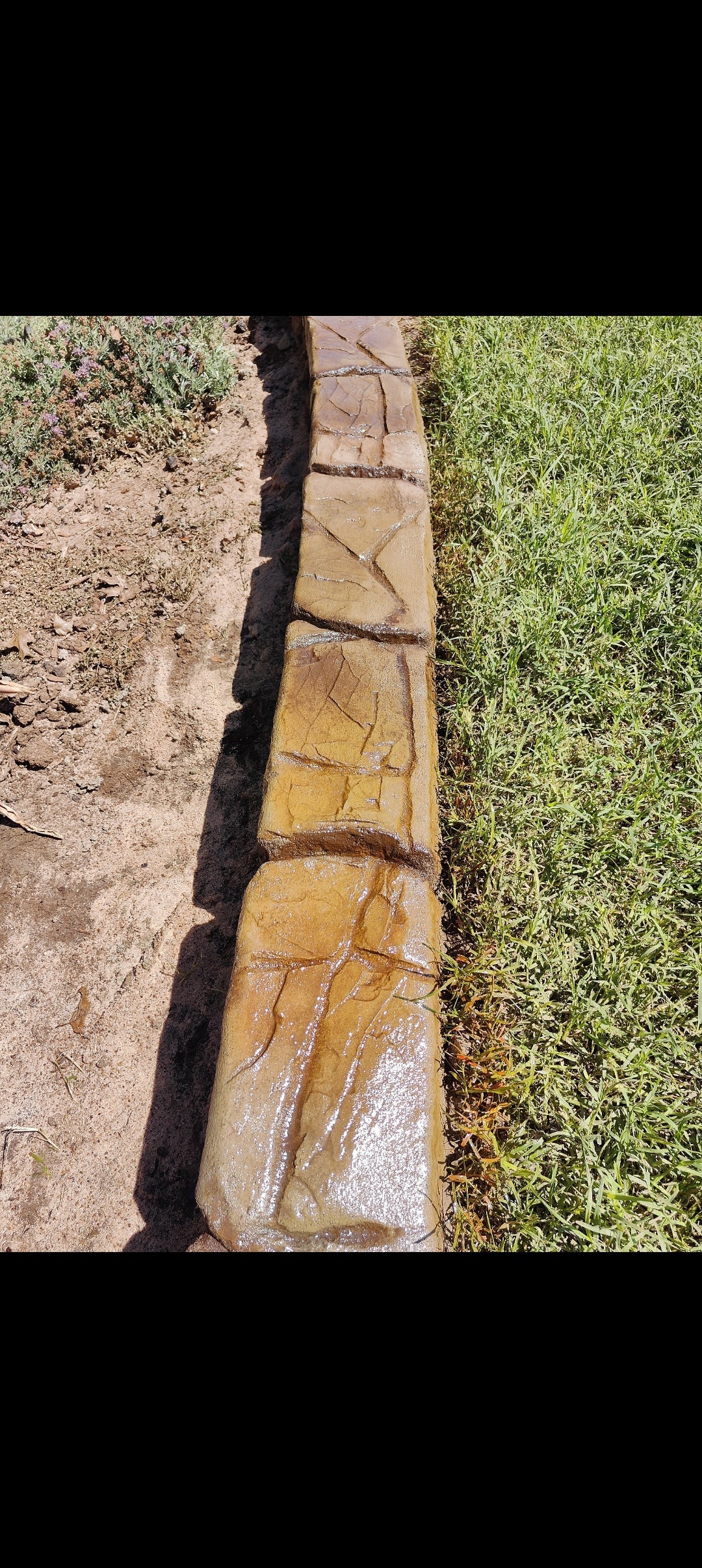 Ransom Canyon slate curb brown and yellowish earth tones in color along some green grass on one side the other side is a flower bed with a green bush in it. top view showing the deep stone like textures with brown joint lines. Curbart Creations