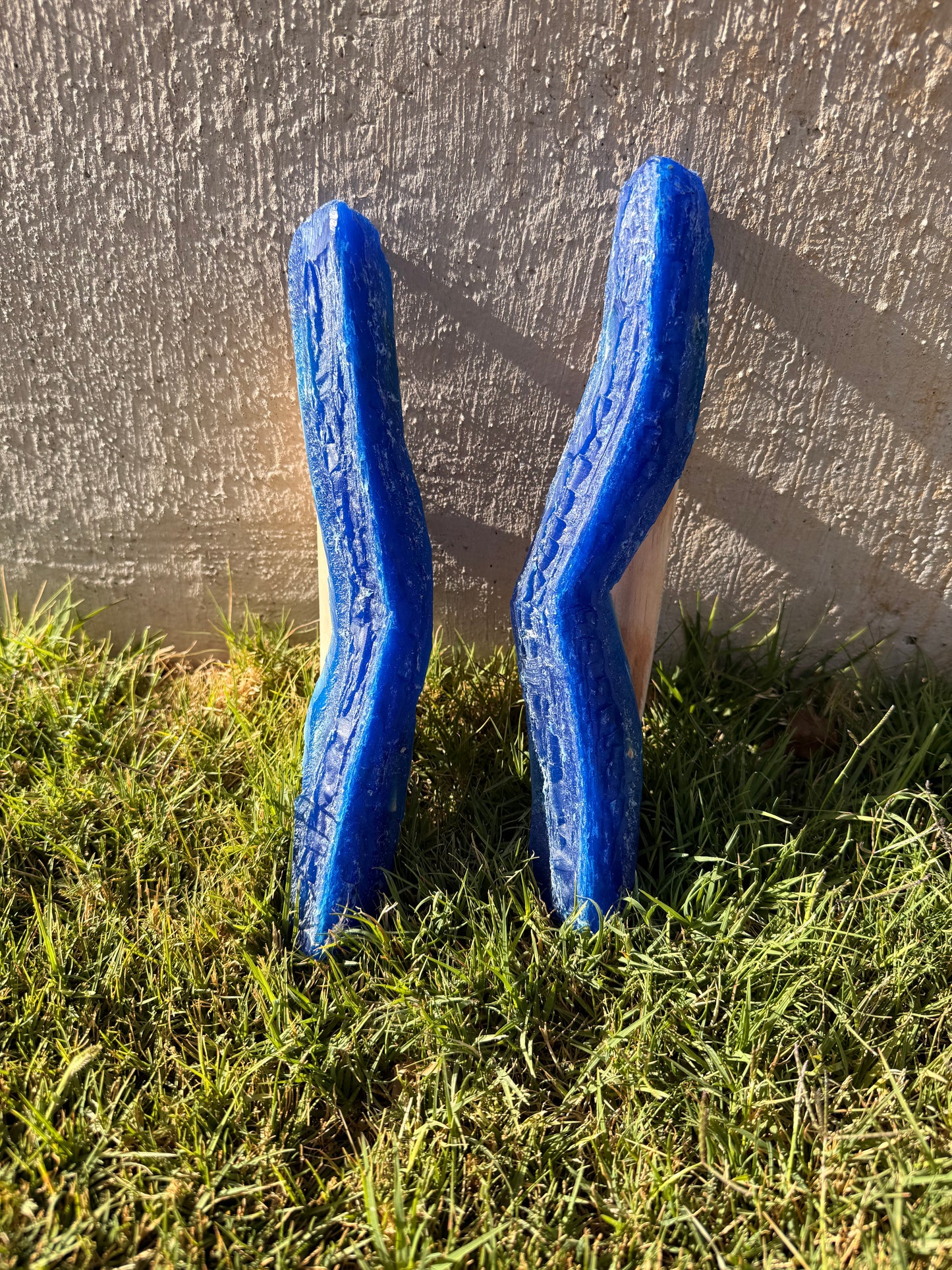 Two blue plastic joint tools on grass against a concrete wall.