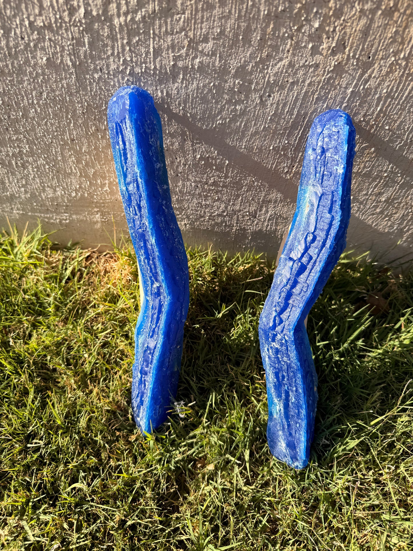 Two blue plastic joint tools on grass with a concrete wall in the background