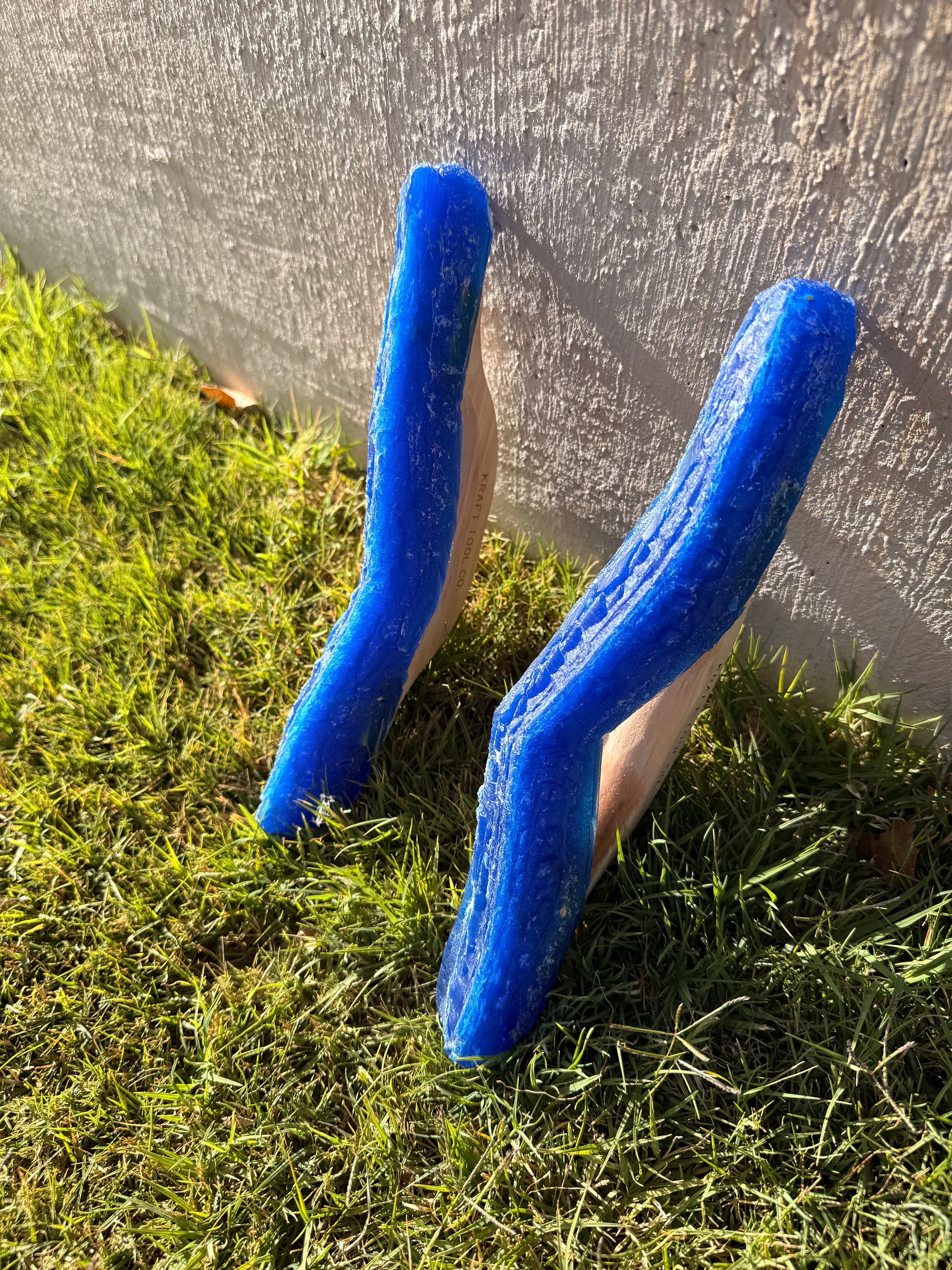 Two blue  joint tools on the grass next to a concrete wall.